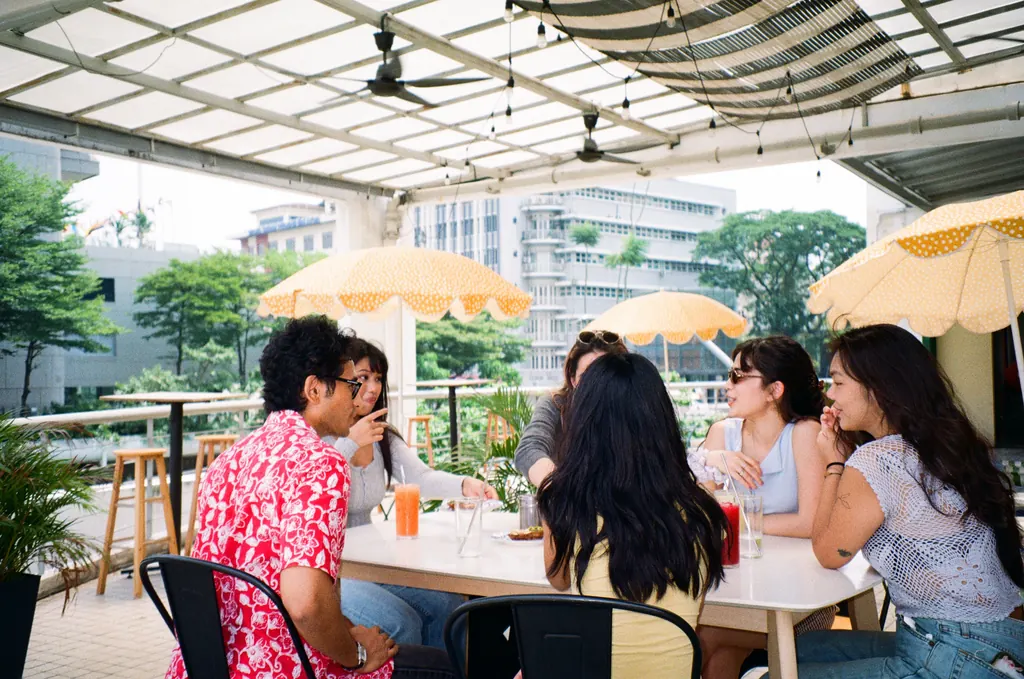 Friends socializing on the Bartolo terrace with umbrellas, drinks and KL skyline